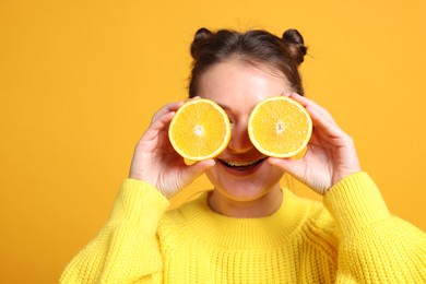 Happy girl holding orange halves near eyes on orange background