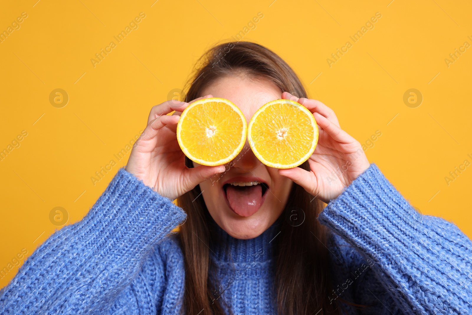 Photo of Happy girl holding orange halves near eyes on orange background