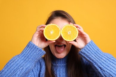 Happy girl holding orange halves near eyes on orange background