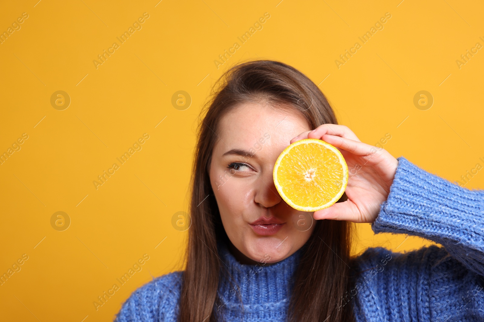 Photo of Young woman holding orange half near eye on orange background