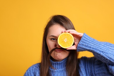 Young woman holding orange half near eye on orange background