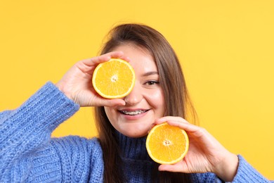 Photo of Happy young woman with orange halves on yellow background