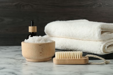 Photo of Spa treatment. Towels, sea salt, brush and bottle of serum on white marble table, closeup