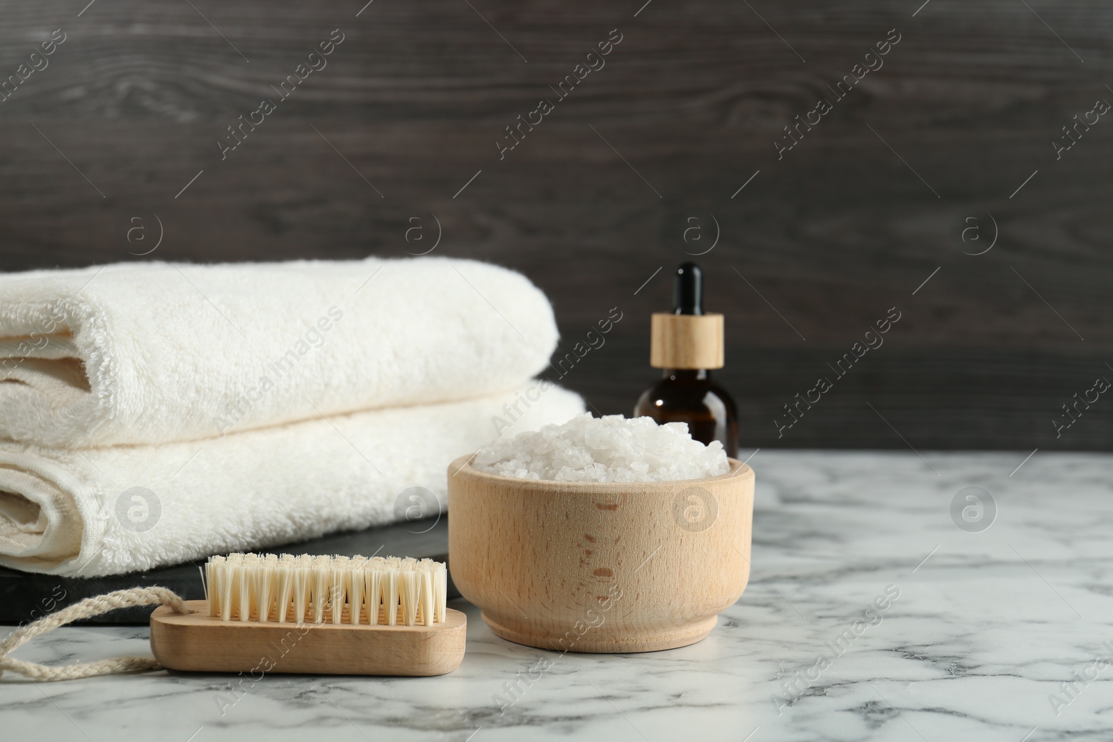 Photo of Spa treatment. Towels, sea salt, brush and bottle of serum on white marble table, space for text