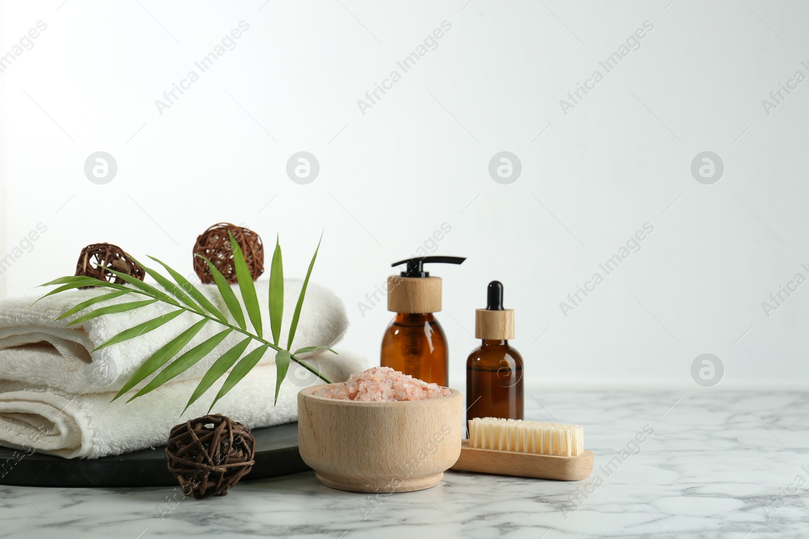 Photo of Spa treatment. Towels, sea salt, brush, bottles of cosmetic products and palm leaf on white marble table, space for text