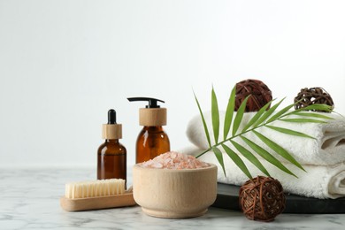 Photo of Spa treatment. Towels, sea salt, brush, bottles of cosmetic products and palm leaf on white marble table