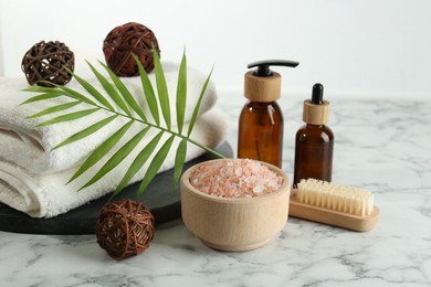 Photo of Spa treatment. Towels, sea salt, brush, bottles of cosmetic products and palm leaf on white marble table