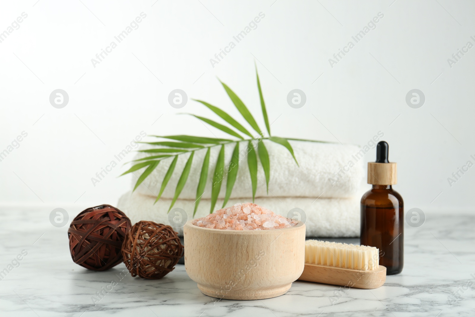 Photo of Spa treatment. Towels, sea salt, brush, bottle of serum and palm leaf on white marble table