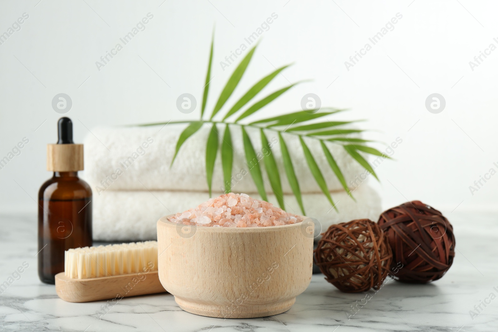 Photo of Spa treatment. Towels, sea salt, brush, bottle of serum and palm leaf on white marble table, closeup