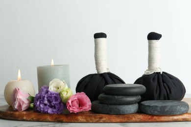 Photo of Massage bags, spa stones, burning candles and beautiful flowers on white marble table