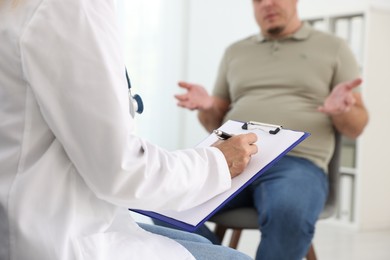 Nutritionist with clipboard consulting overweight man in clinic, closeup