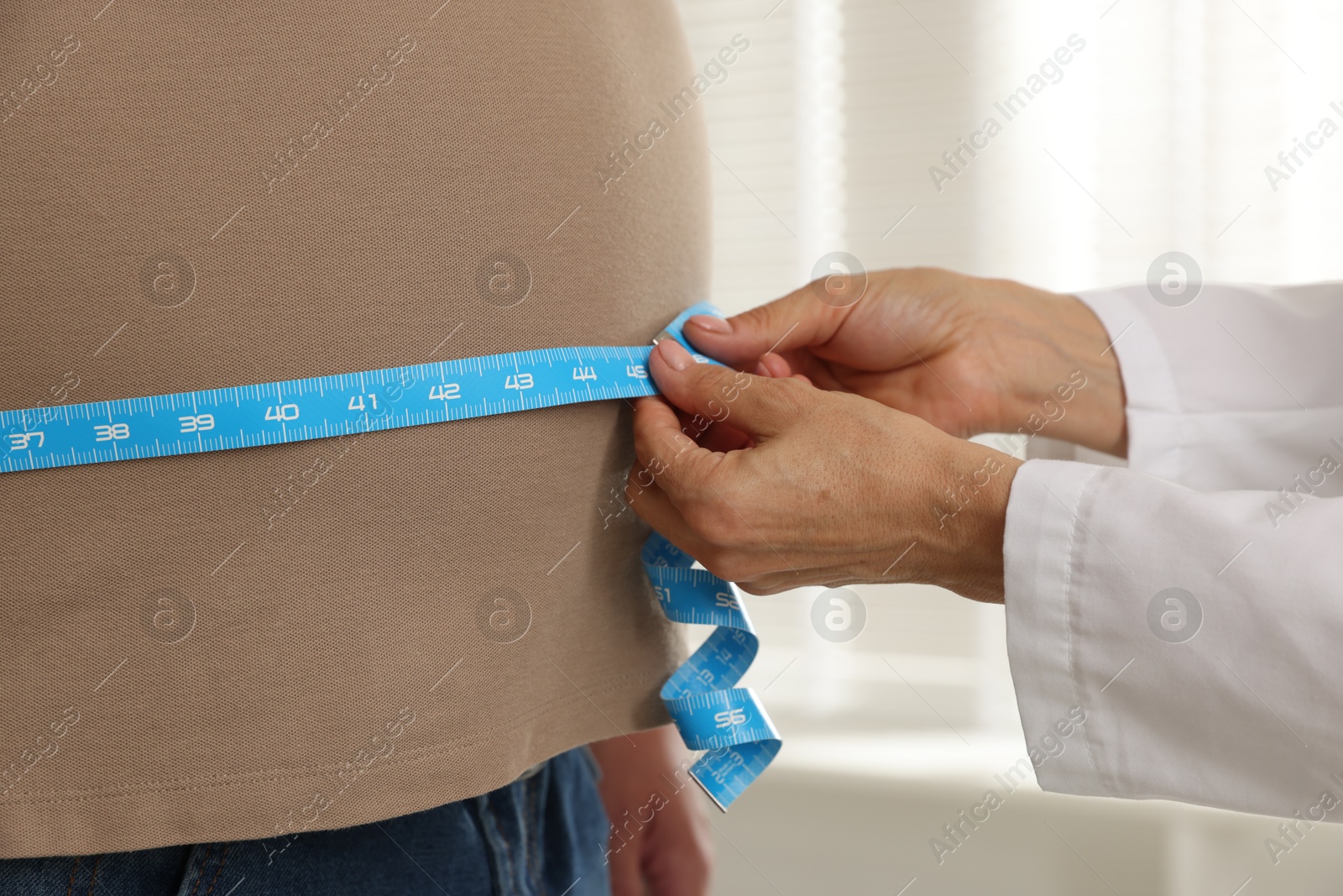 Photo of Nutritionist measuring overweight man's waist with tape in clinic, closeup