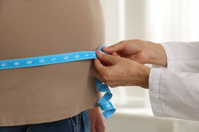 Photo of Nutritionist measuring overweight man's waist with tape in clinic, closeup