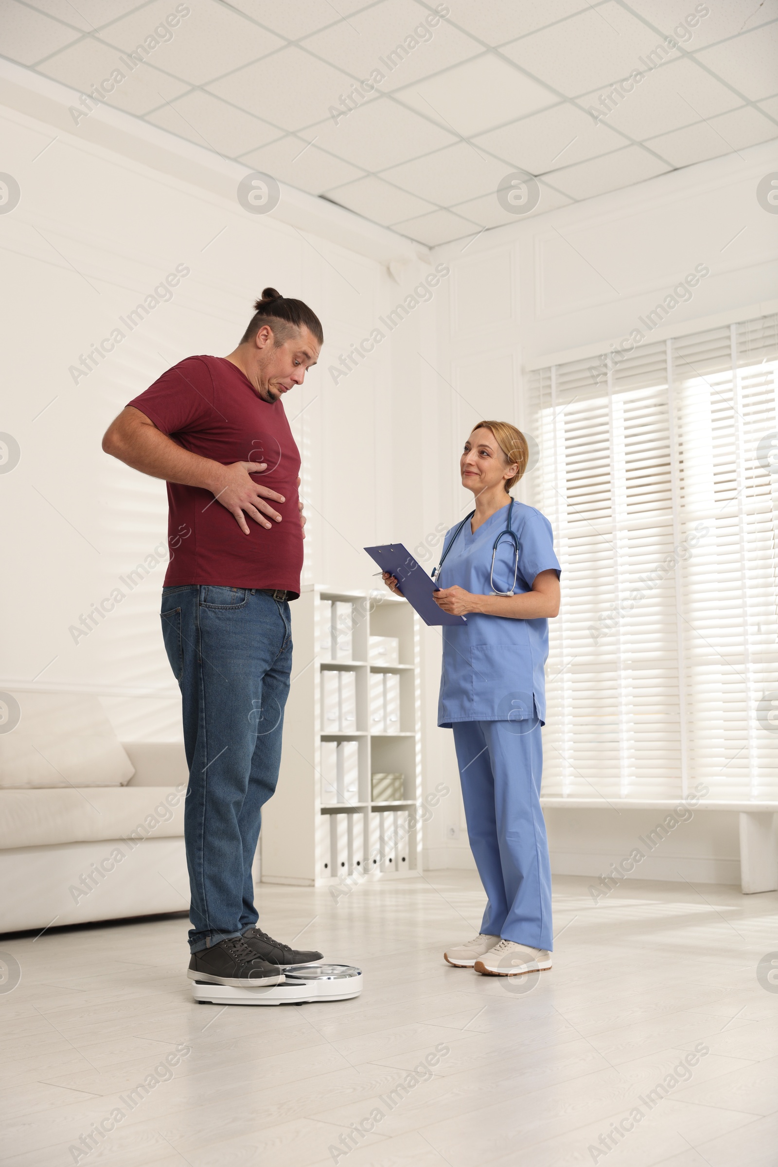 Photo of Overweight man standing on scales during consultation with nutritionist in clinic