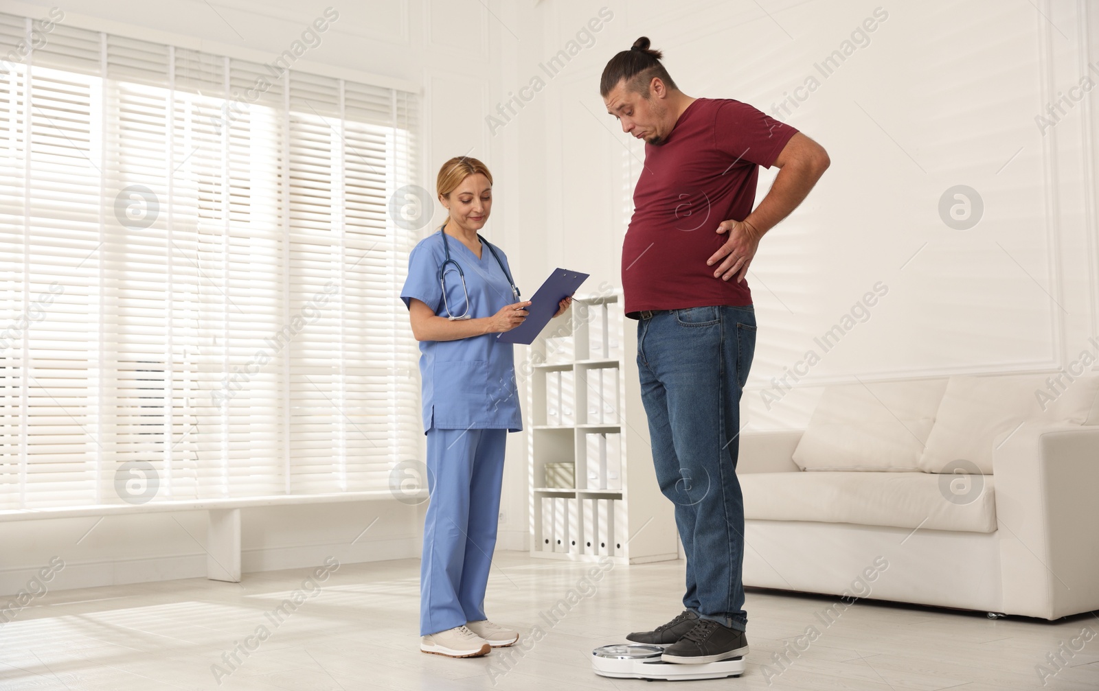 Photo of Overweight man standing on scales during consultation with nutritionist in clinic