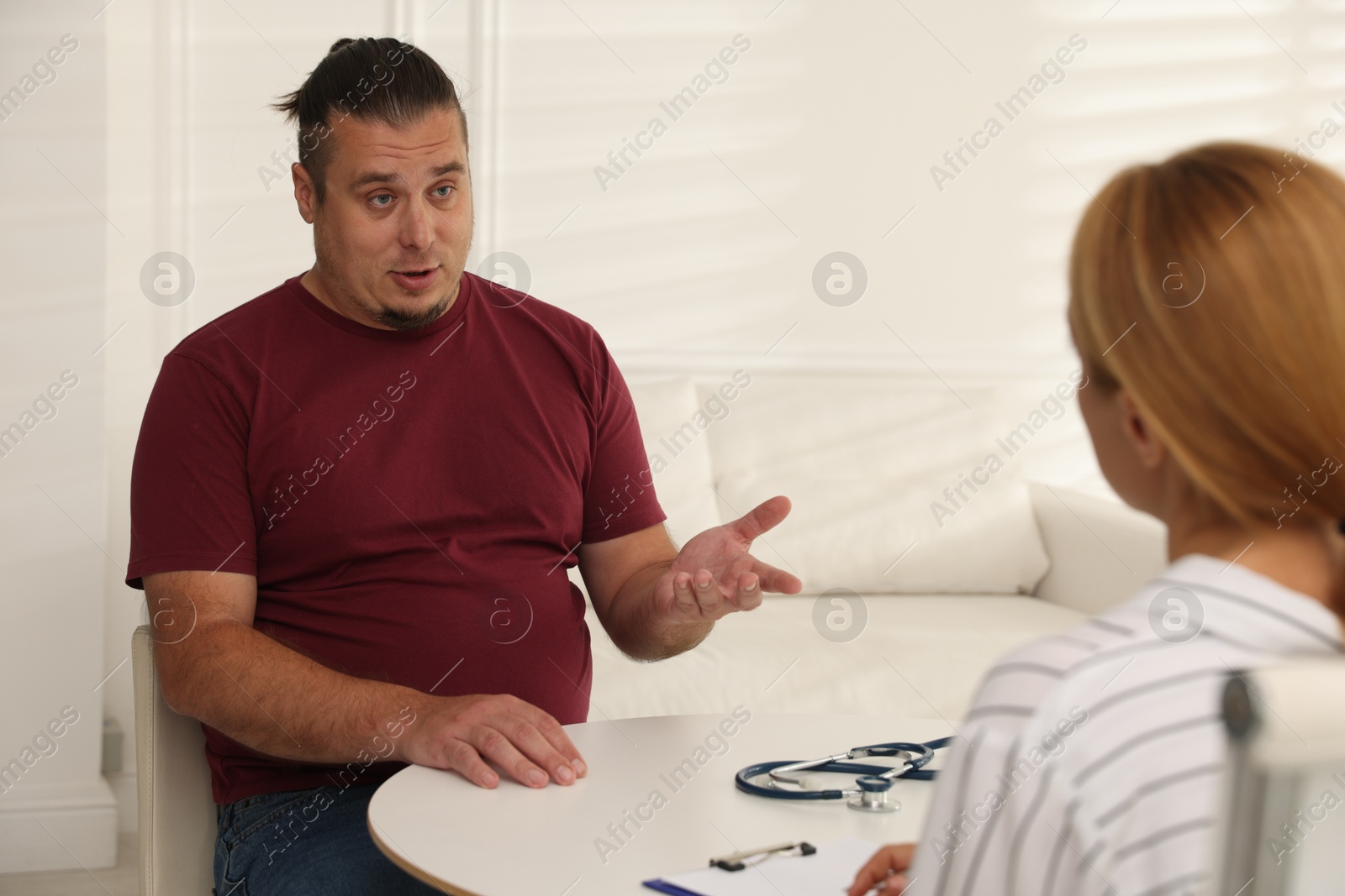 Photo of Overweight man having consultation with nutritionist at table in clinic