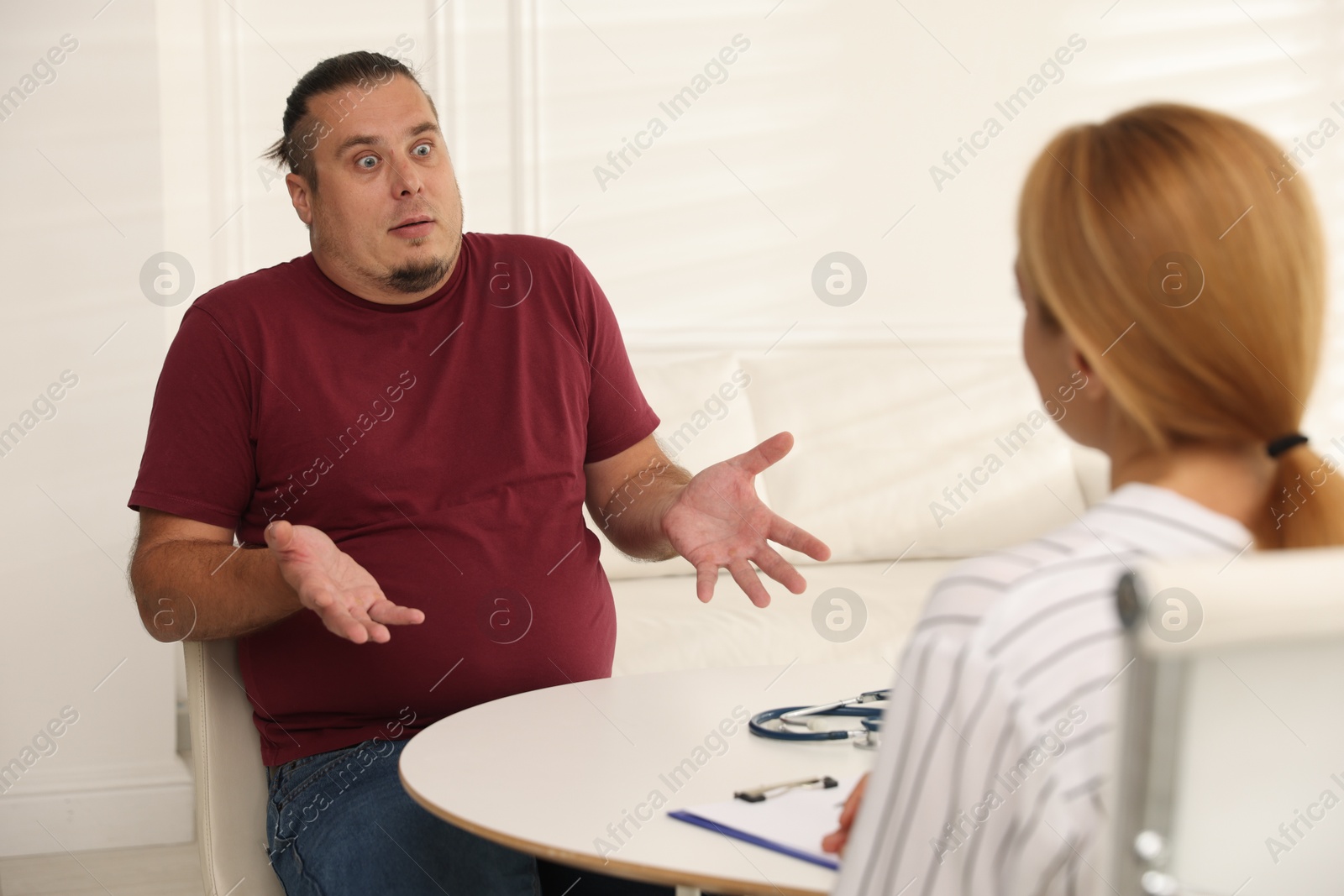 Photo of Overweight man having consultation with nutritionist at table in clinic