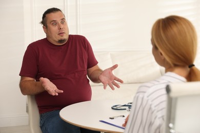 Photo of Overweight man having consultation with nutritionist at table in clinic