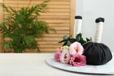 Photo of Spa treatment. Massage bags and beautiful flowers on white table, space for text