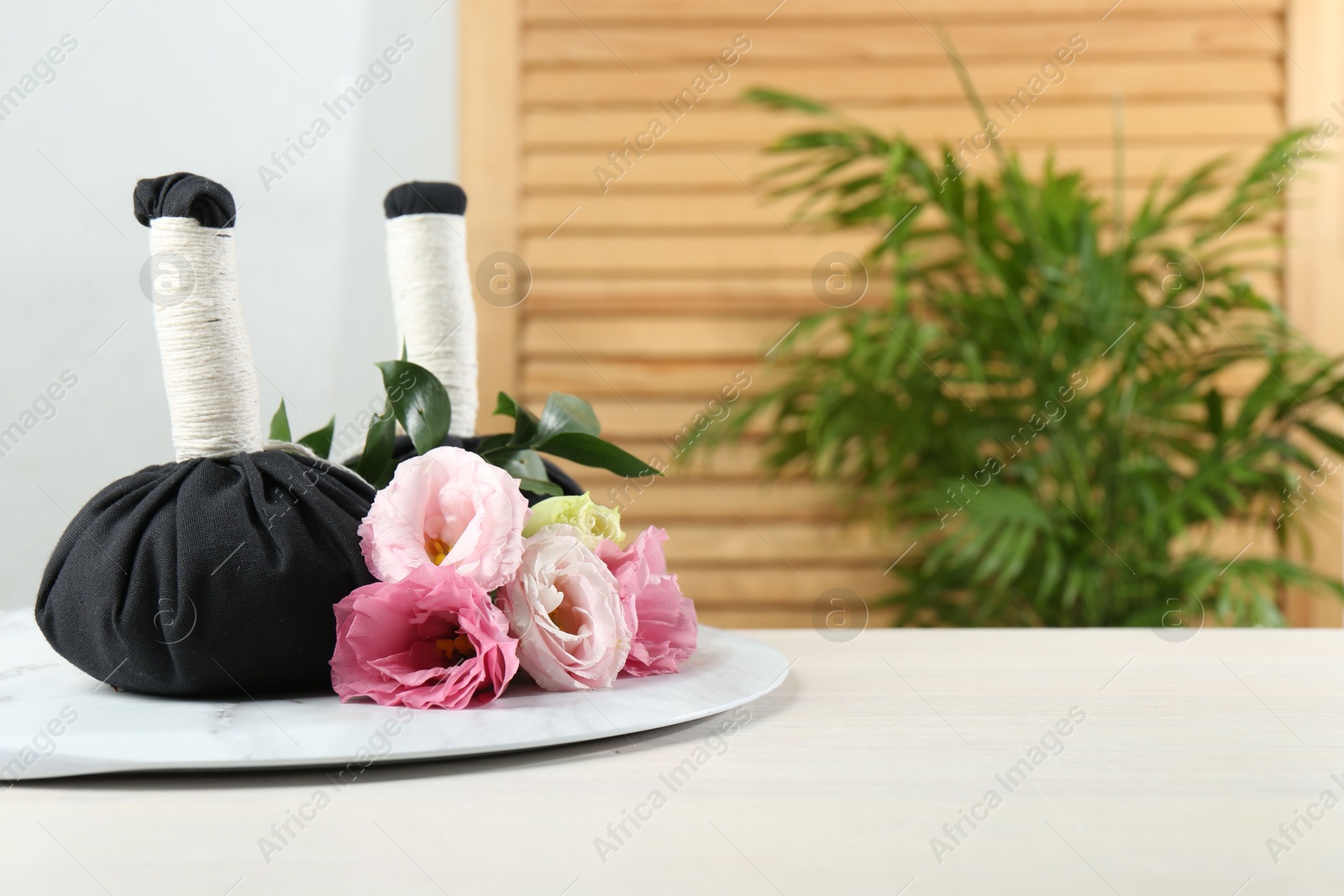 Photo of Spa treatment. Massage bags and beautiful flowers on white table, space for text