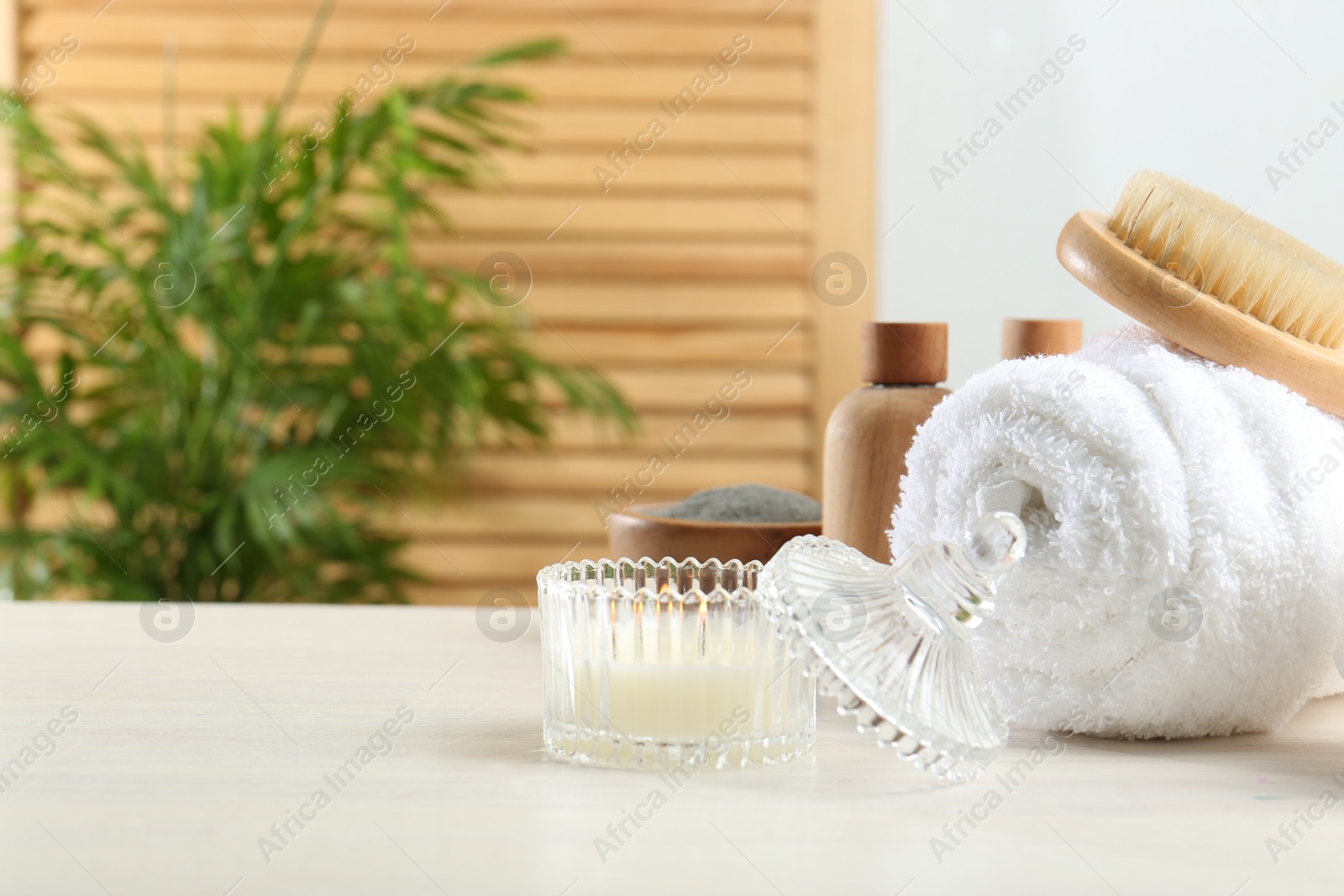 Photo of Spa treatment. Towel, brush, cosmetic products and candle on white table, space for text