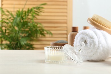 Photo of Spa treatment. Towel, brush, cosmetic products and candle on white table, space for text