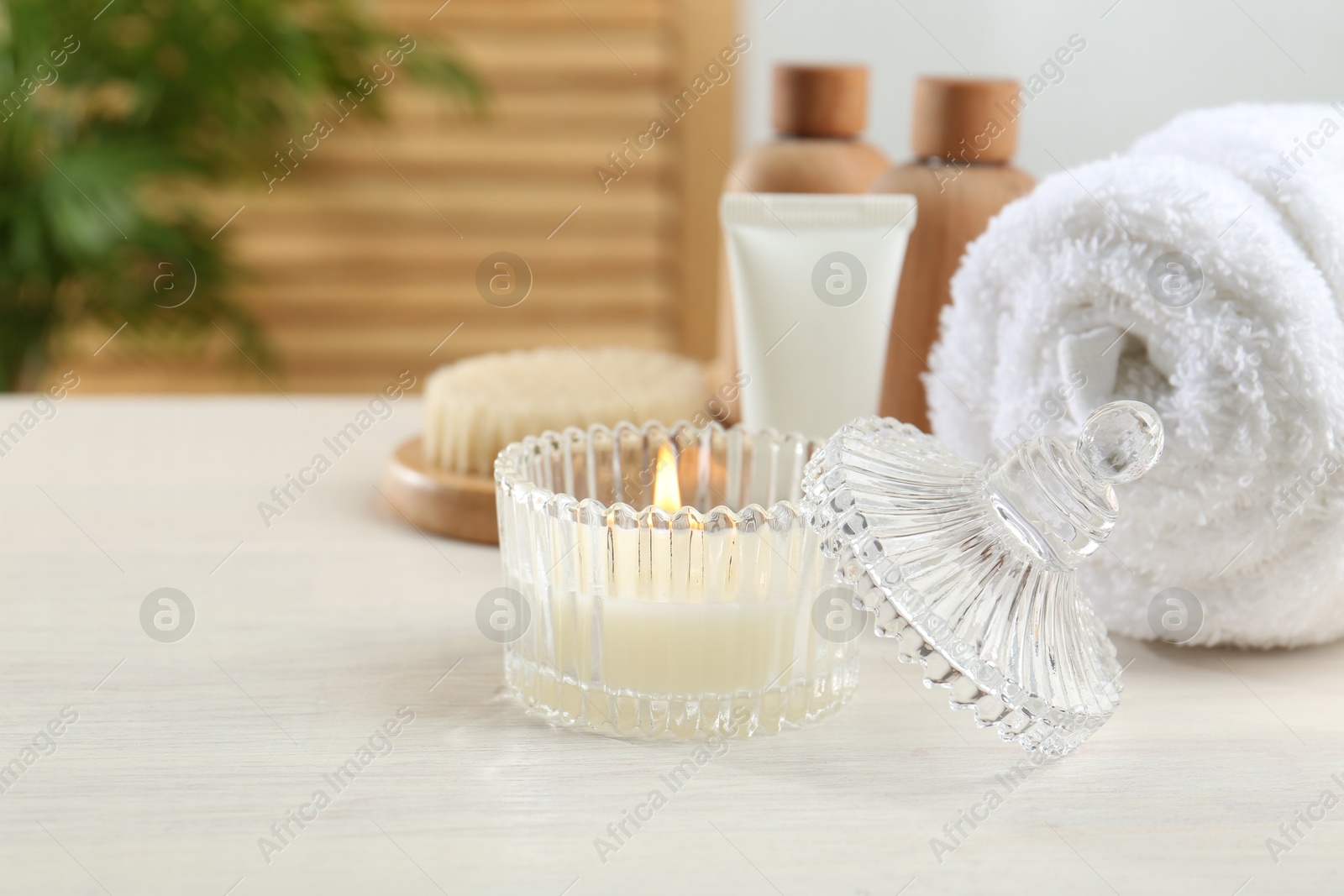 Photo of Spa treatment. Towel, cosmetic products and candle on white table, space for text