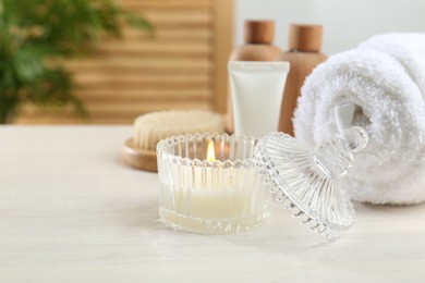 Spa treatment. Towel, cosmetic products and candle on white table, space for text