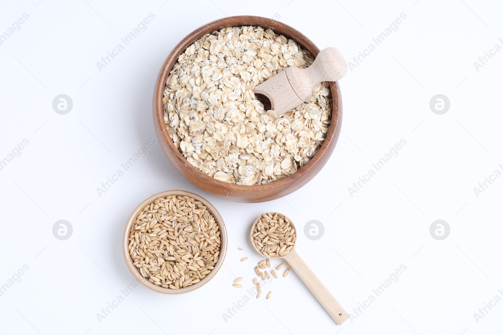 Photo of Oat flakes in bowl, grains, scoop and spoon isolated on white, top view