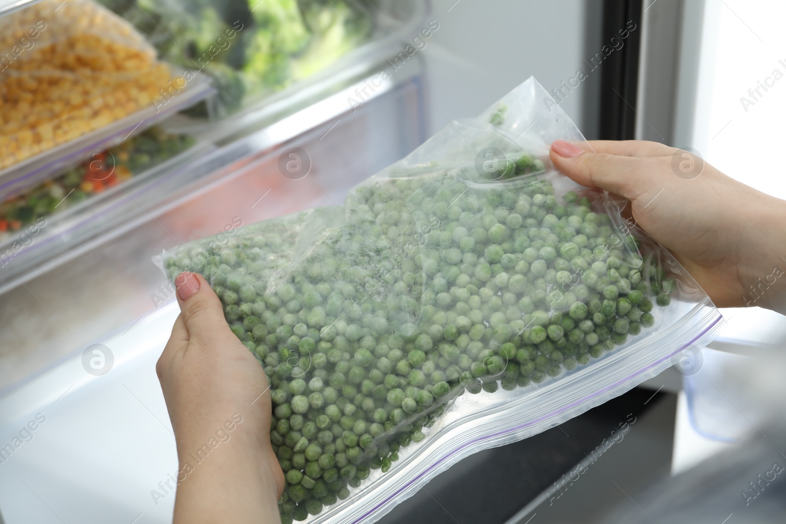 Photo of Woman taking plastic bag with frozen green peas from refrigerator, closeup