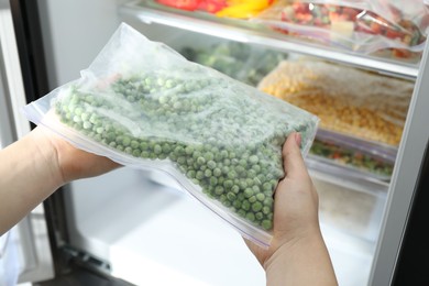 Photo of Woman taking plastic bag with frozen green peas from refrigerator, closeup