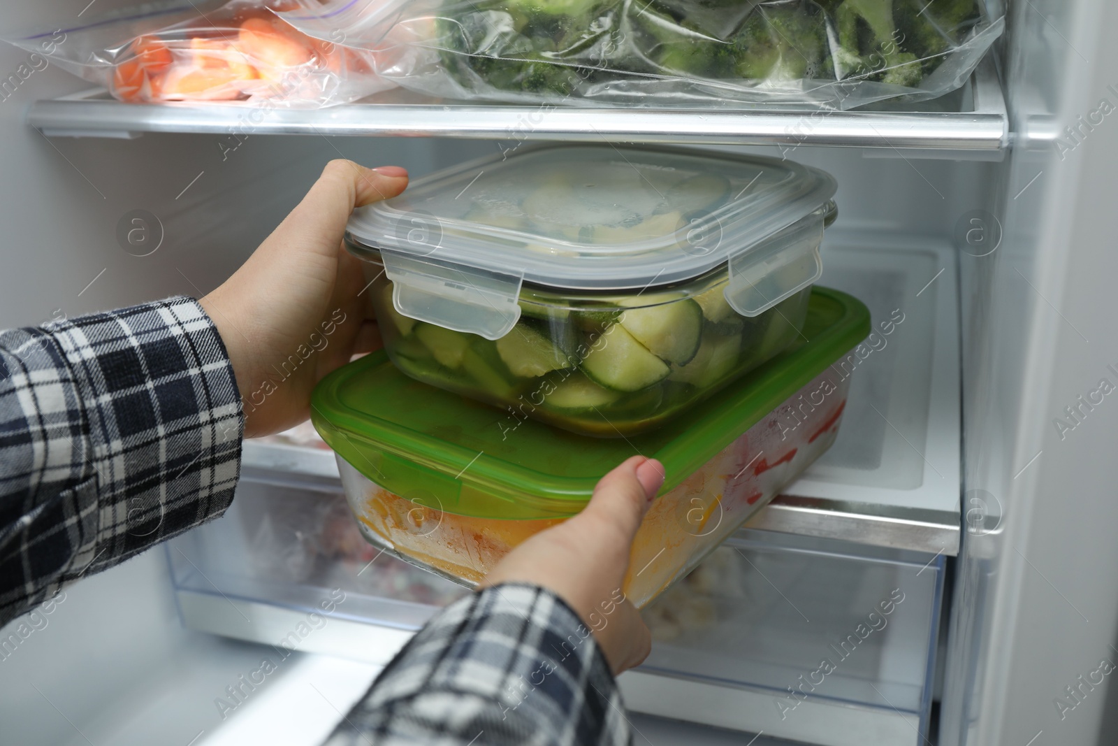 Photo of Woman taking glass containers with frozen vegetables from refrigerator, closeup