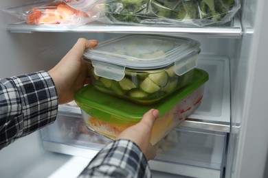 Photo of Woman taking glass containers with frozen vegetables from refrigerator, closeup