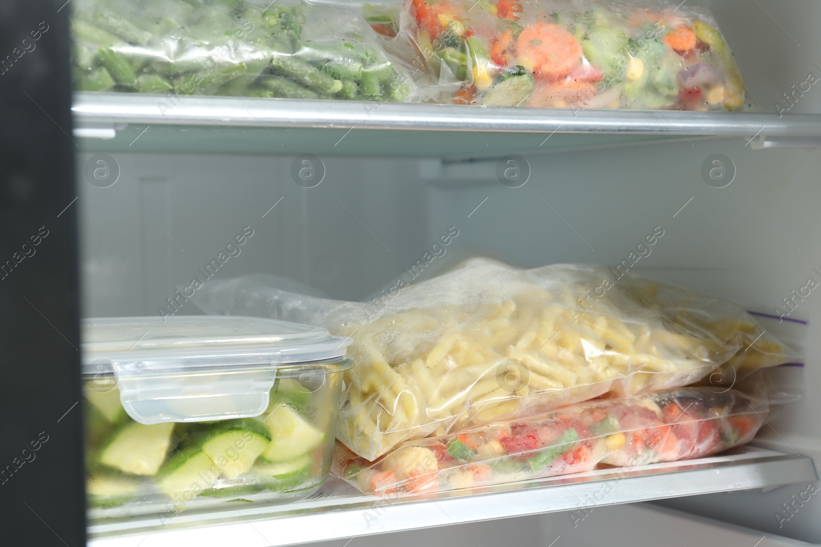 Photo of Plastic bags and glass container with different frozen vegetables in refrigerator, closeup