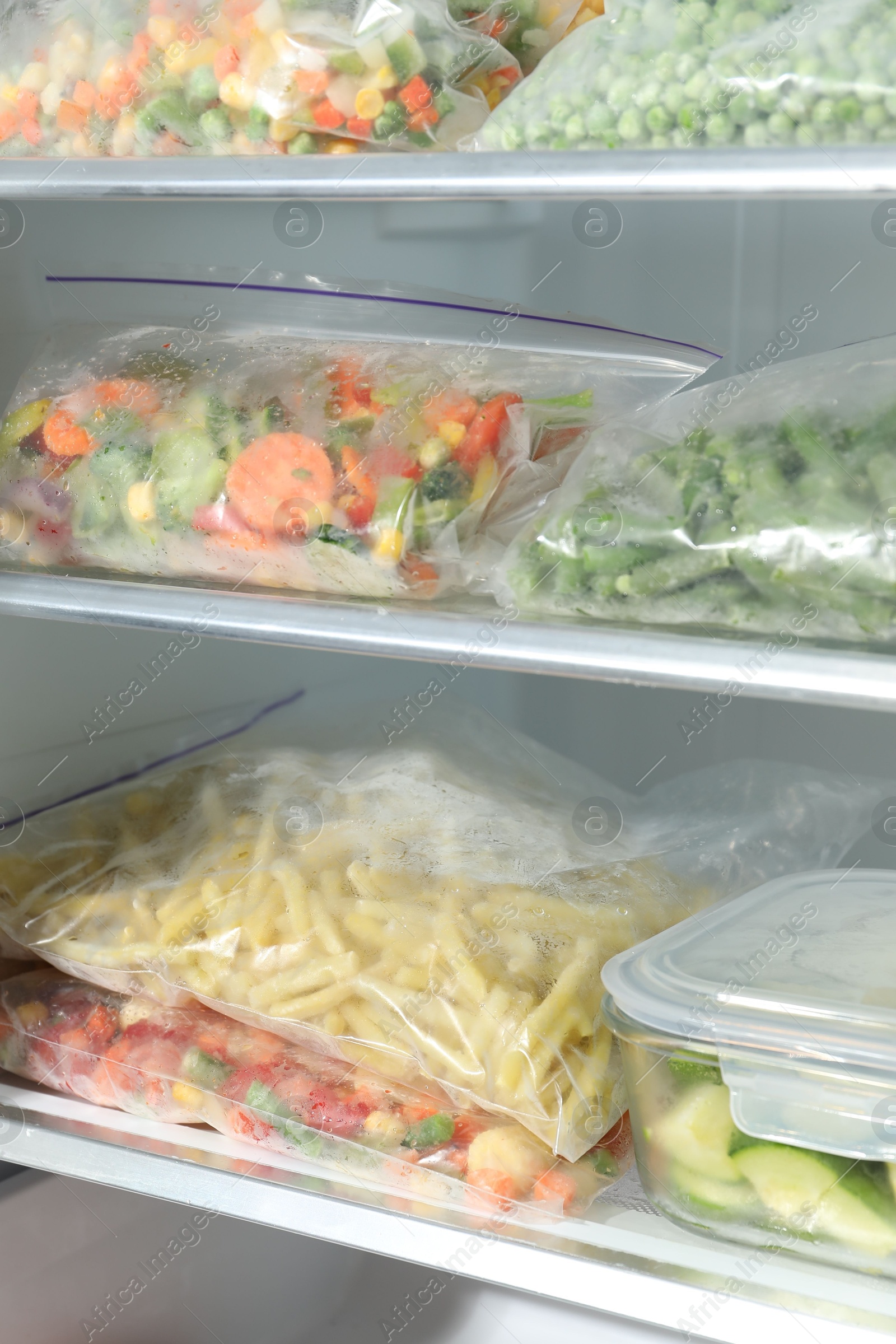 Photo of Plastic bags and glass container with different frozen vegetables in refrigerator, closeup