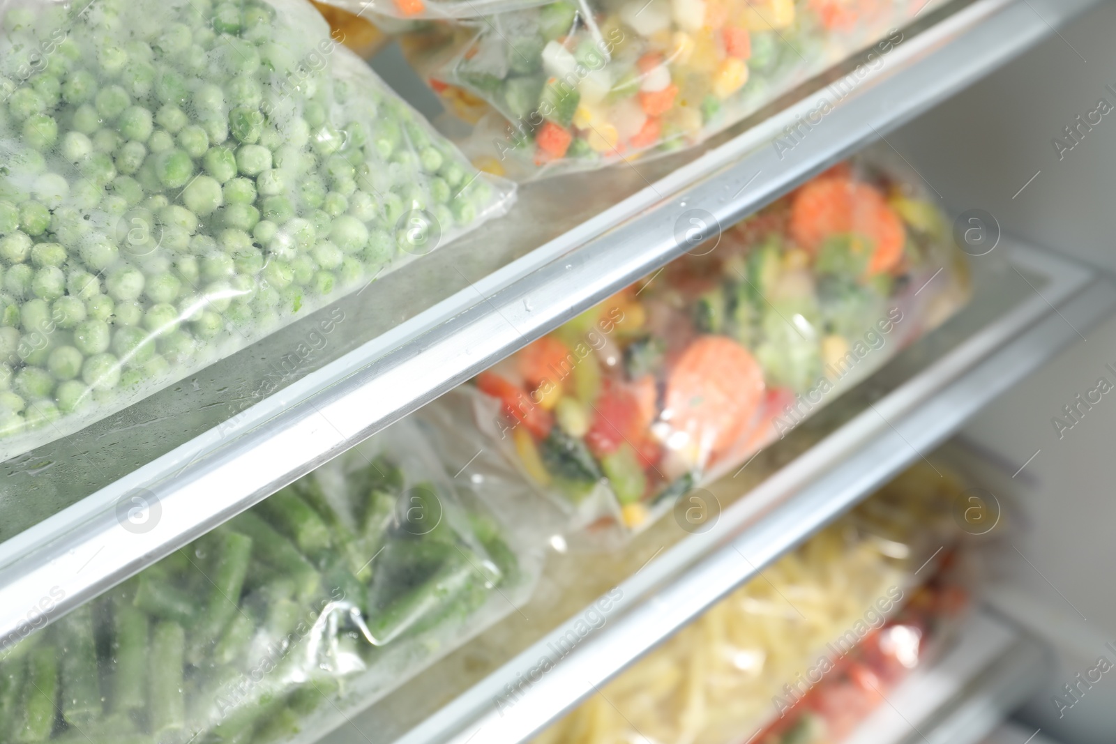 Photo of Plastic bags with different frozen vegetables in refrigerator, closeup