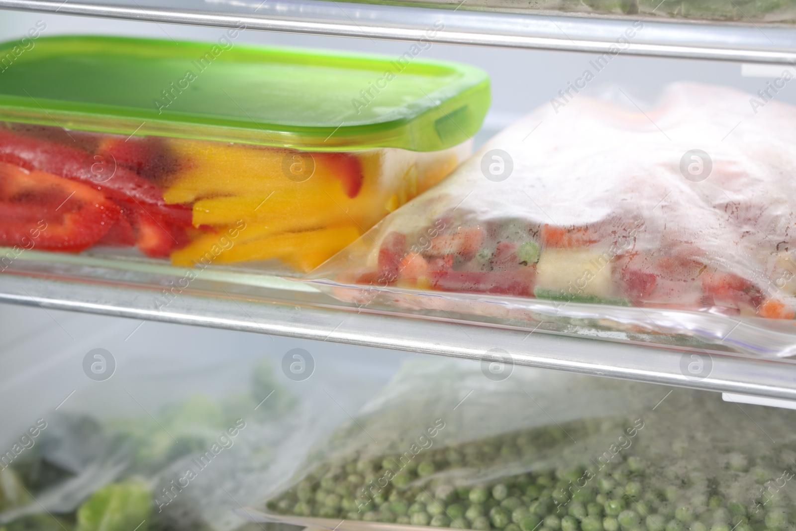 Photo of Plastic bags and glass container with different frozen vegetables in refrigerator, closeup