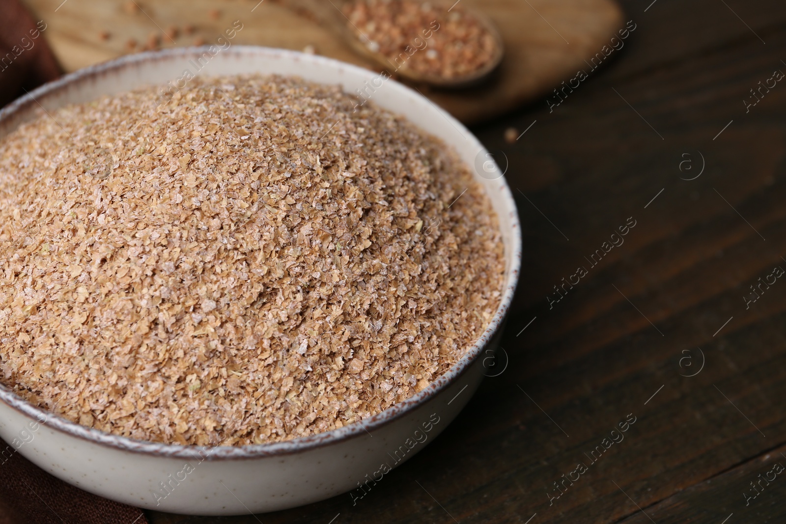 Photo of Buckwheat bran in bowl on wooden table, closeup. Space for text