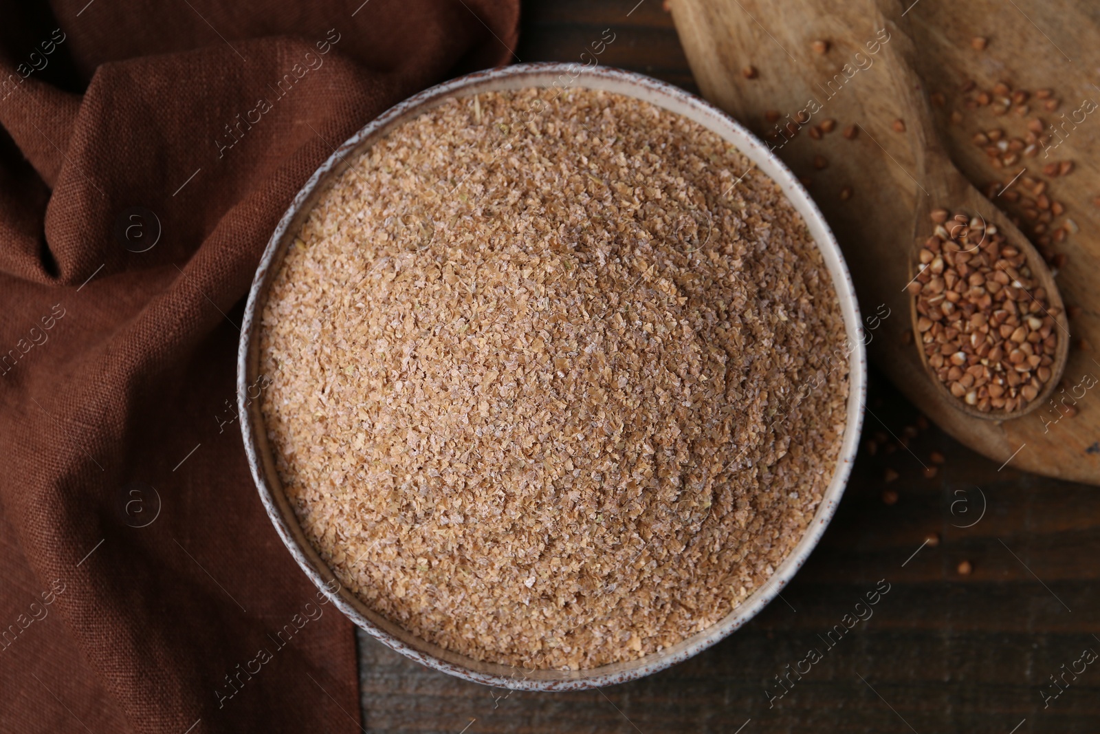 Photo of Buckwheat bran in bowl and grains on wooden table, top view