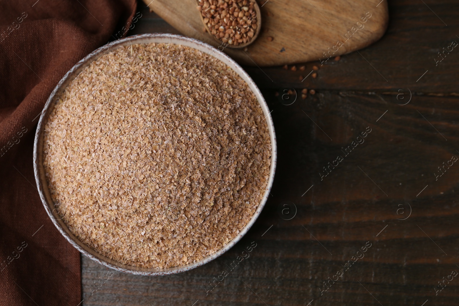 Photo of Buckwheat bran in bowl and grains on wooden table, top view. Space for text