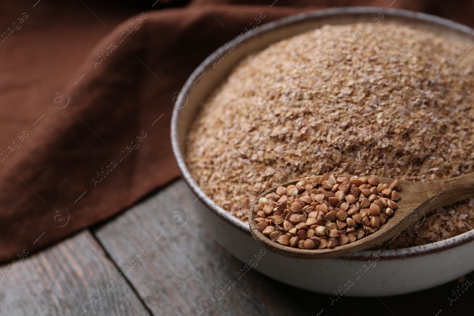 Photo of Buckwheat bran in bowl and grains on wooden table, closeup. Space for text