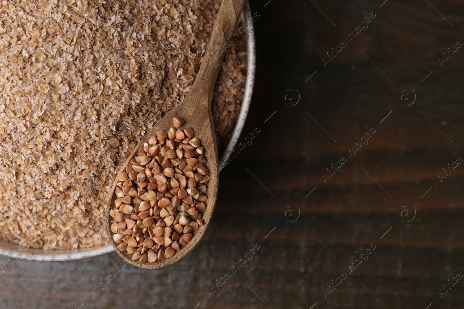 Photo of Buckwheat bran in bowl and grains on wooden table, top view. Space for text