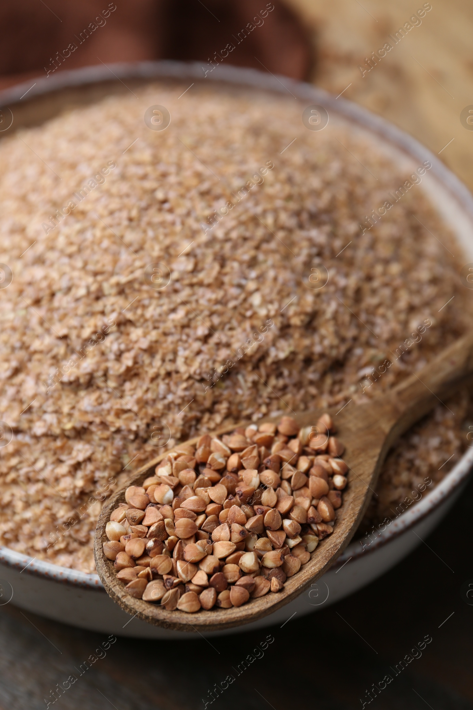 Photo of Buckwheat bran in bowl and grains on table, closeup