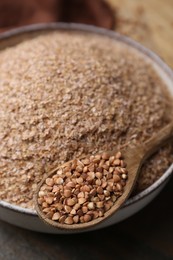 Photo of Buckwheat bran in bowl and grains on table, closeup