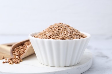 Photo of Buckwheat bran in bowl and grains on white marble table, closeup