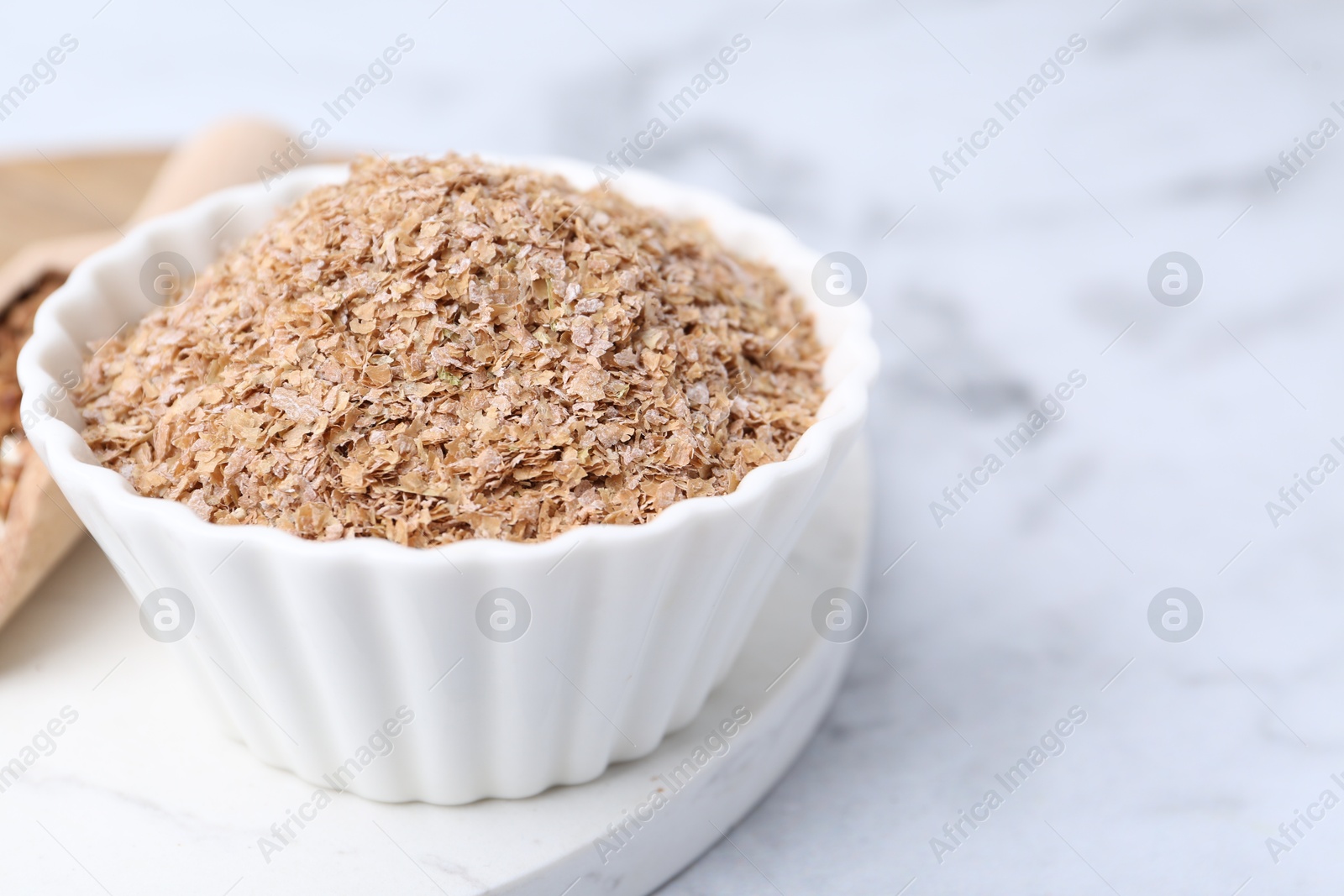 Photo of Buckwheat bran in bowl on white marble table, closeup. Space for text