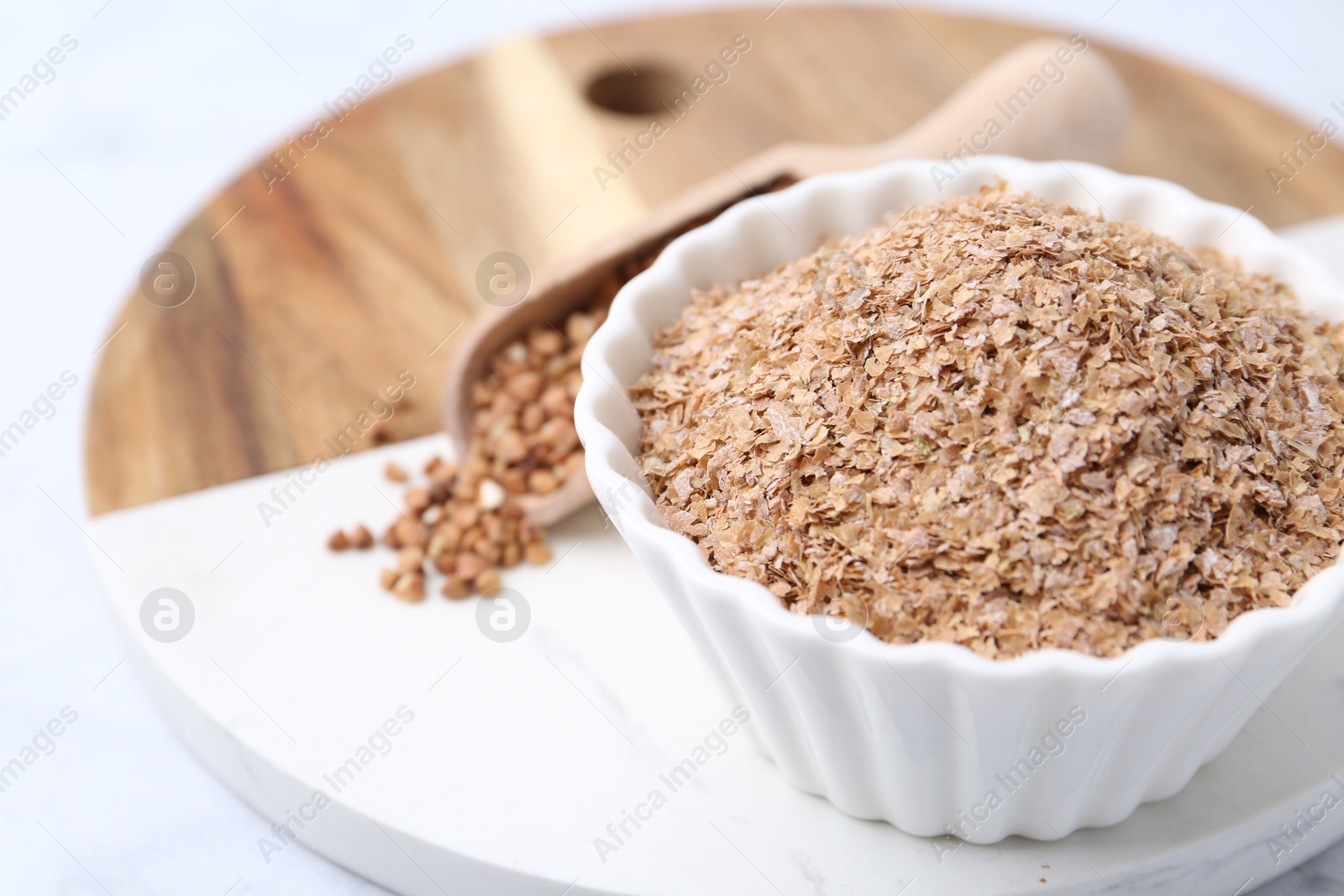 Photo of Buckwheat bran in bowl on white table, closeup. Space for text