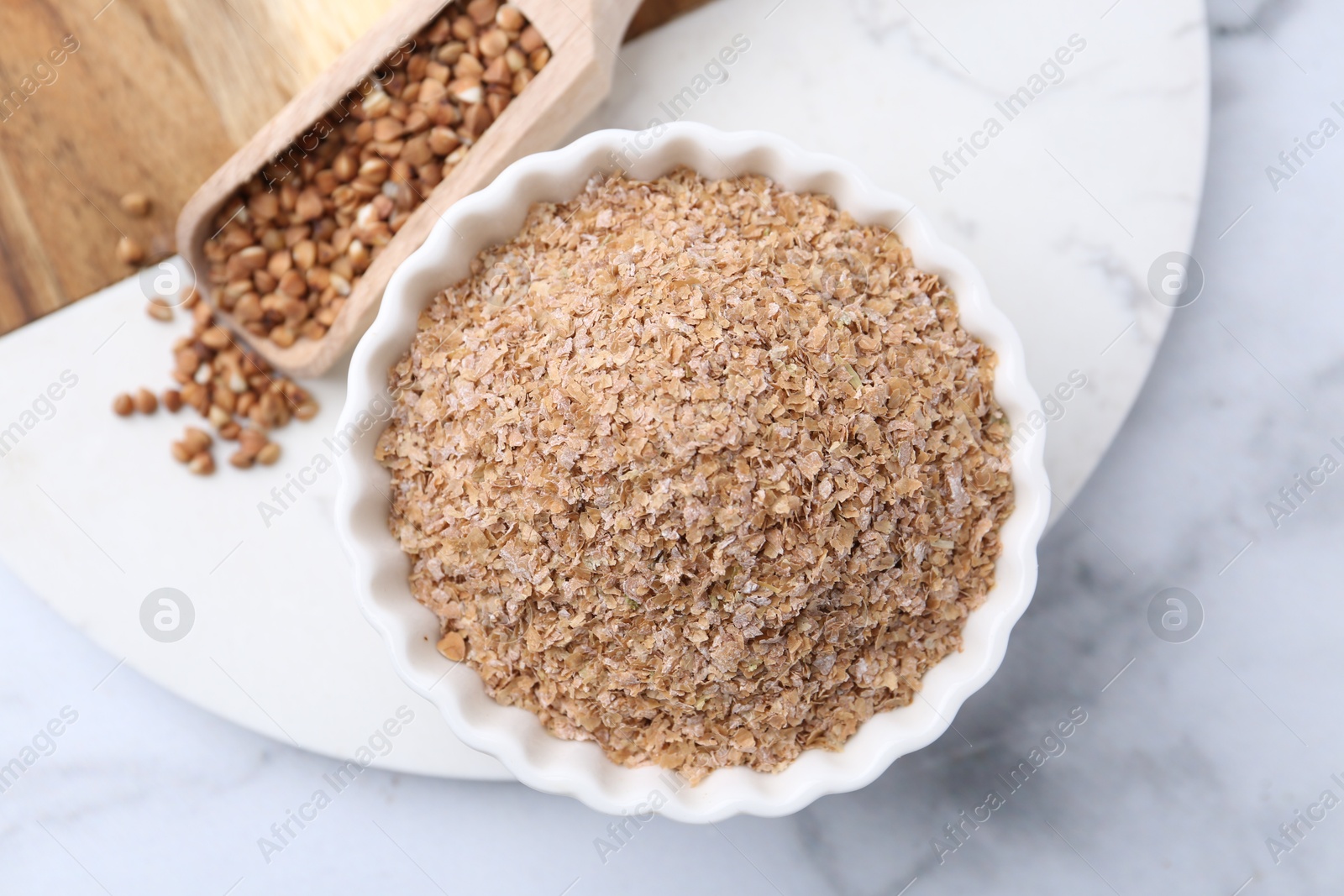 Photo of Buckwheat bran in bowl and grains on white marble table, top view