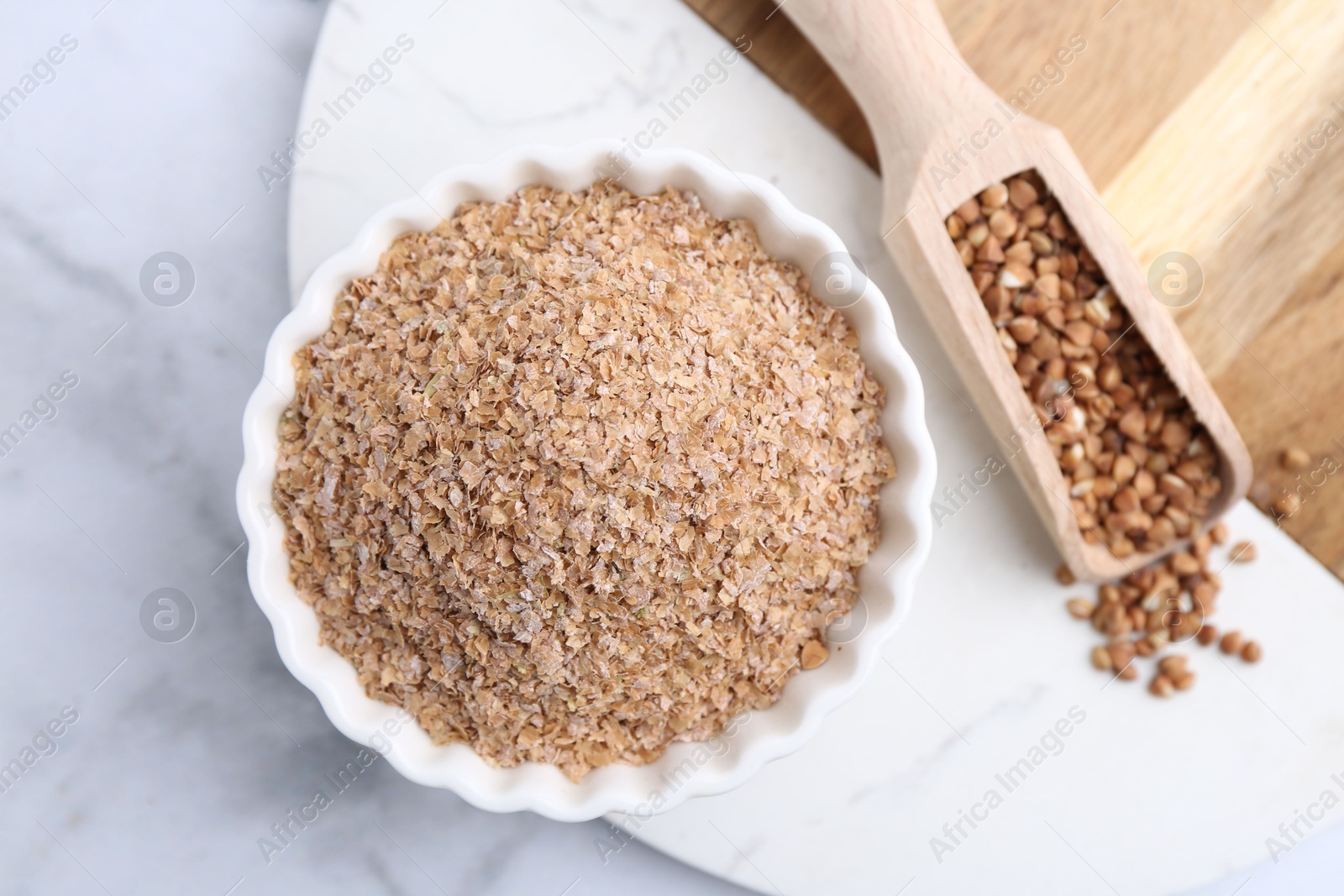 Photo of Buckwheat bran in bowl and grains on white marble table, top view