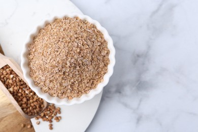 Photo of Buckwheat bran in bowl and grains on white marble table, top view. Space for text